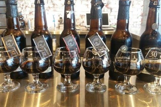 A flight of dark stouts in branded glasses, lined up in front of matching beer bottles