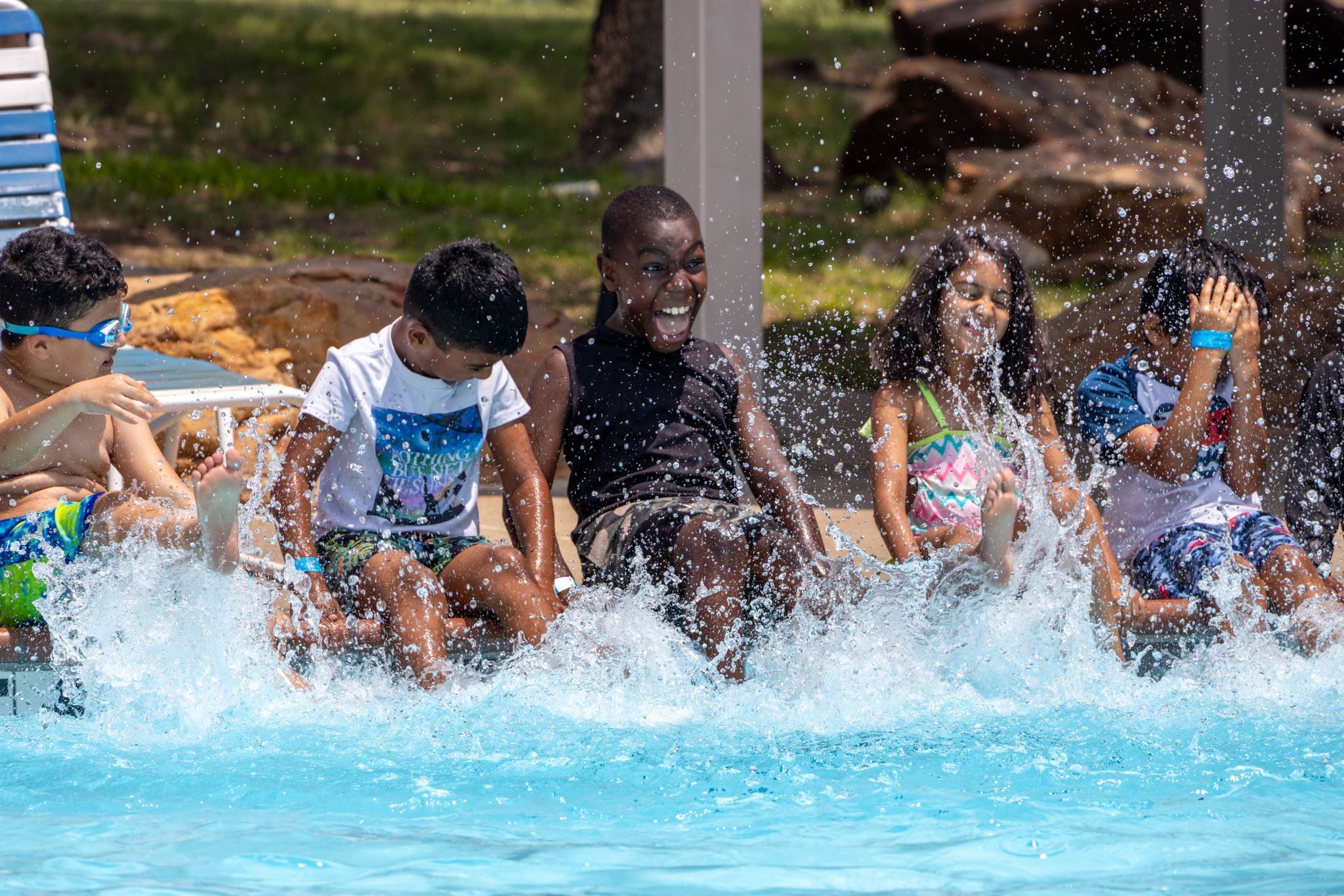 Children laughing and splashing water while sitting on the edge of a swimming pool.