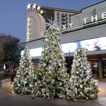 Holiday trees with silver decorations light up the plaza outside Galaxy Theatre at dusk.